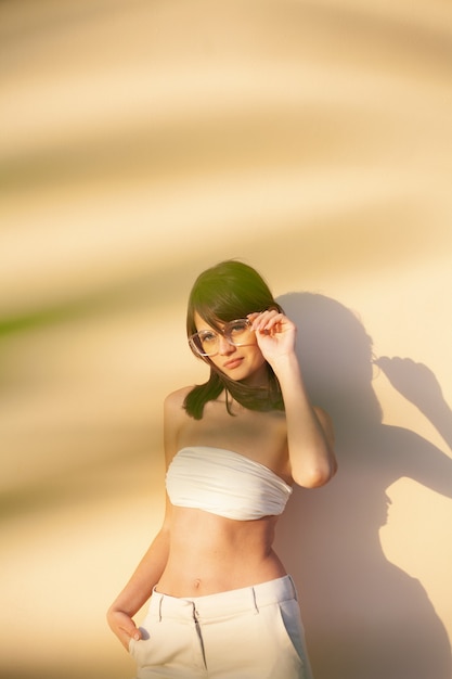 Chica elegante con gafas de sol cubiertas con una sombra de una rama sobre un fondo beige
