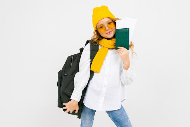 Chica elegante con una mochila sobre los hombros tiene un pasaporte con boletos de vacaciones sobre un fondo blanco con espacio de copia.