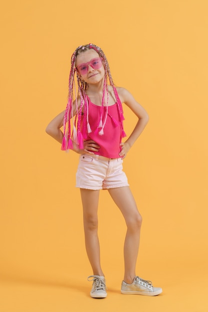 Chica elegante con rastas rosas posando sobre un fondo amarillo