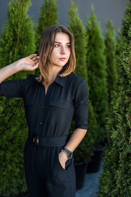 Chica en un elegante vestido negro posando entre agujas de pino y disfrutando de un cálido día soleado