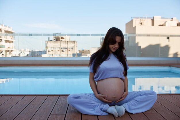 Chica embarazada cerca de la piscina sosteniendo su primer plano del estómago