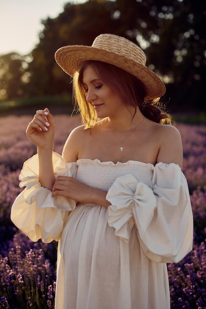 La chica embarazada con un sombrero en el campo de lavanda al atardecer