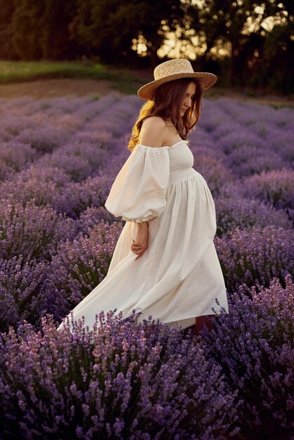 La chica embarazada con un sombrero en el campo de lavanda al atardecer