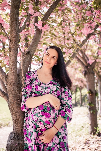 Chica embarazada con un vestido cerca de la sakura en el jardín.