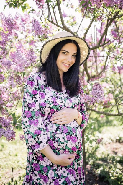 Una chica embarazada con un vestido cerca de la sakura en el jardín.