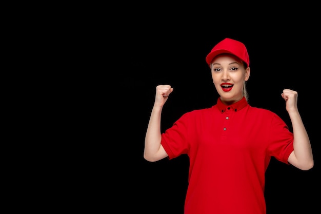 Chica emocionada del día de la camisa roja sosteniendo los puños en una gorra roja con camisa y lápiz labial brillante