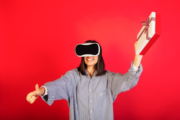 Chica emocionada feliz positiva en gafas de realidad virtual VR con caja de regalo, sonriendo con alegría y mostrando un gesto genial