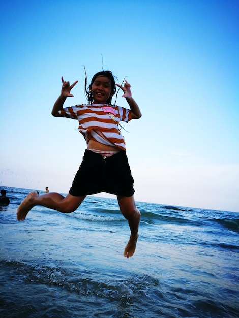 Foto chica emocionada saltando por la orilla contra el cielo despejado