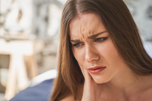 Chica emocional. Mujer joven encantada negativa tocando su mejilla mientras hace cara de dolor. Concepto de cuidado