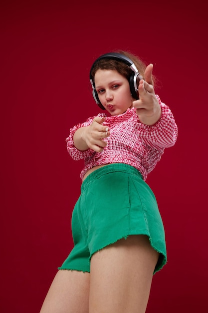 Chica emocional en shorts verdes con auriculares escuchando música inalterada