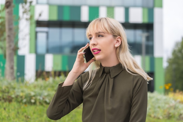 Chica empresaria rubia caucásica en un parque empresarial haciendo una llamada con el teléfono