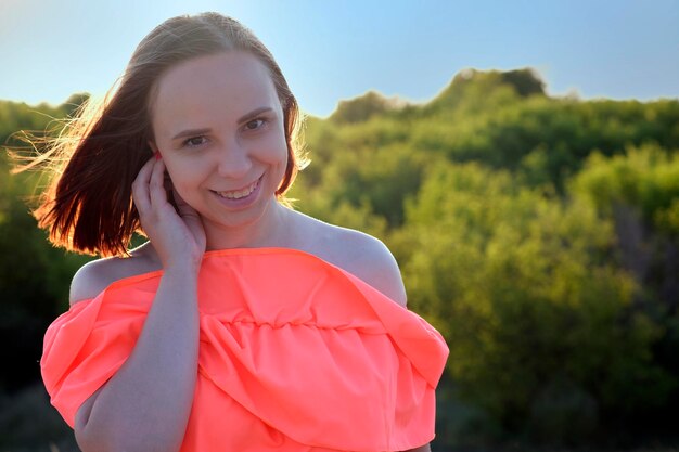 Chica encantadora al atardecer Mujer joven positiva en vestido naranja de pie en un campo de hierba en un día soleado en el campo