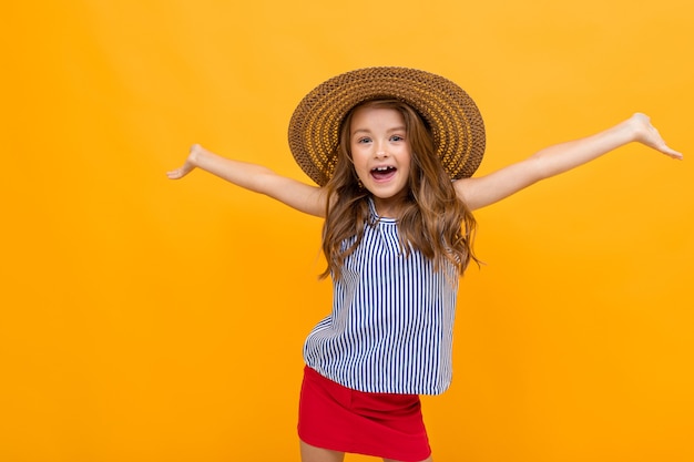 Chica encantadora alegre con un sombrero de paja de verano sobre un fondo amarillo brillante.