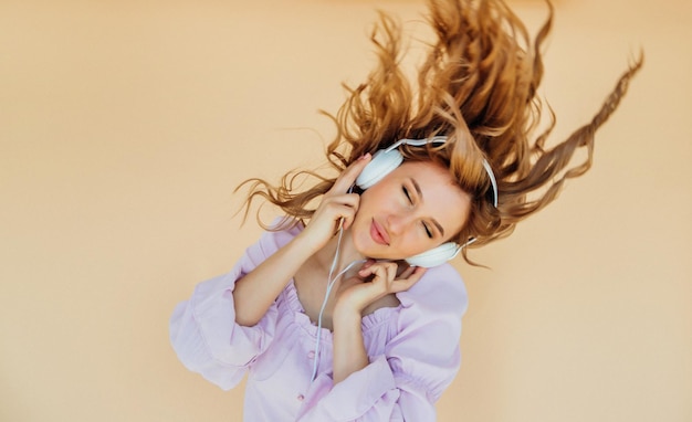 Una chica encantadora con auriculares bailando con el pelo y los ojos cerrados.