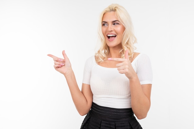 Chica encantadora con una camiseta blanca muestra los dedos a un lado en un blanco con espacio de copia