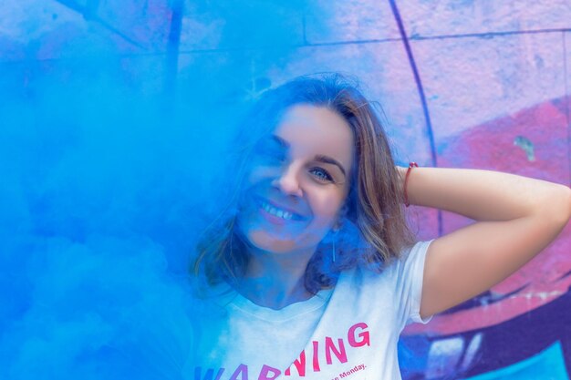 Foto una chica encantadora en humo de colores contra el fondo de graffiti