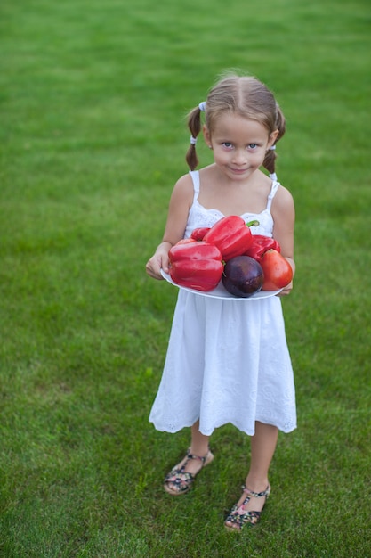 Chica encantadora en un jardín con un plato de verduras