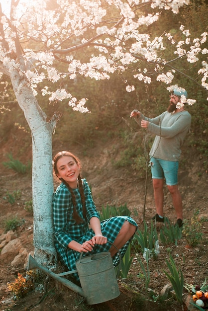 Chica encantadora sonriente en su jardín y mirando plantas de cámara y jardinería como pasatiempo de primavera