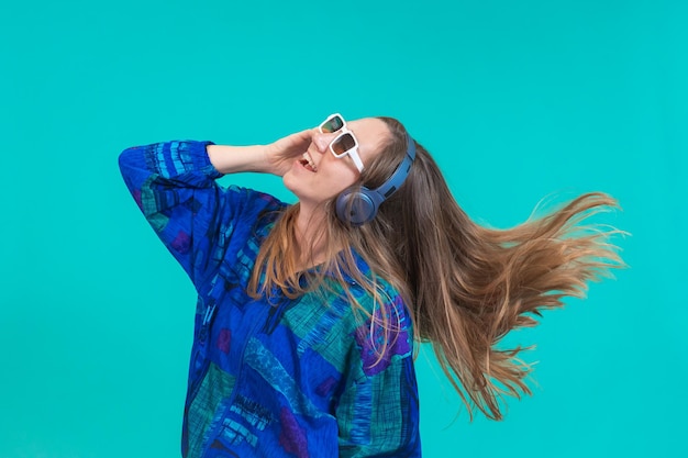 Chica de la energía con auriculares azules escuchando música bailando aislada en un fondo azul en el estudio