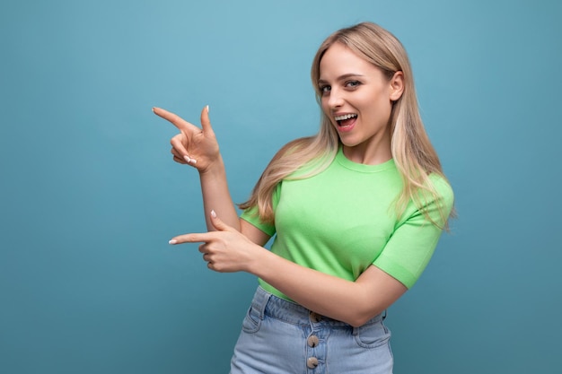 Chica enérgica con ropa informal apuntando a la pared de la izquierda con un fondo azul