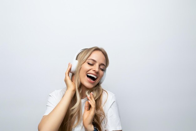 Una chica con entusiasmo y alegría en la cara escucha música con grandes auriculares blancos sobre un fondo blanco.