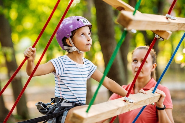 Chica con equipo de escalada en un parque de aventuras se dedica a la escalada en roca o pasa obstáculos en el camino de la cuerda