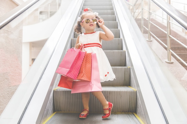 Chica en la escalera mecánica en el centro comercial con compras