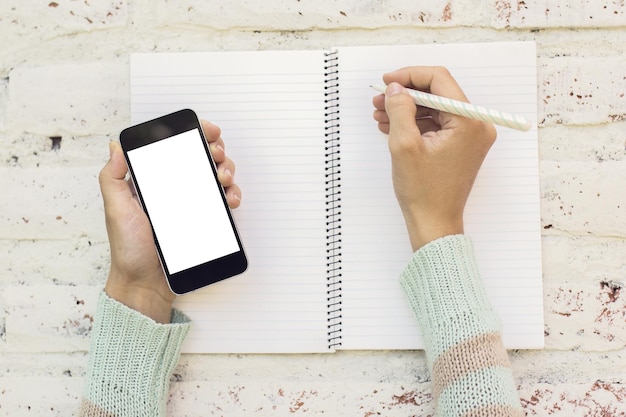 Chica escribe en un diario con maqueta de teléfono celular en blanco