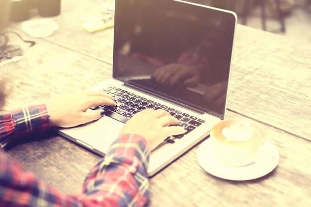 Chica escribiendo con laptop y capuchino en una mesa de madera