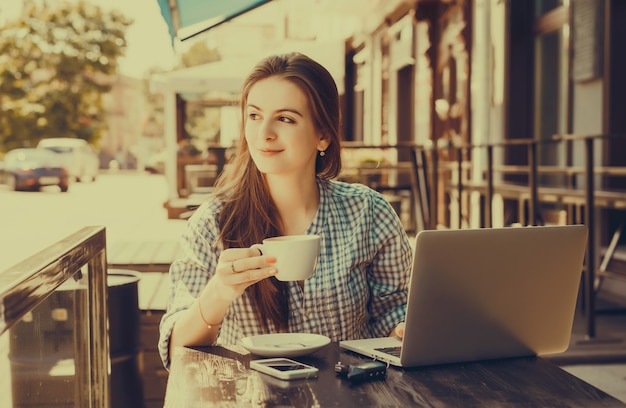 Chica escribiendo en un portátil mientras sujeta una taza de café