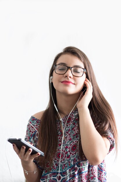 Chica escuchando música con auriculares en el teléfono celular con fondo blanco.