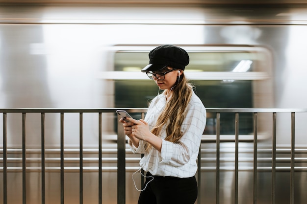 Chica escuchando música mientras espera un tren en una plataforma de metro