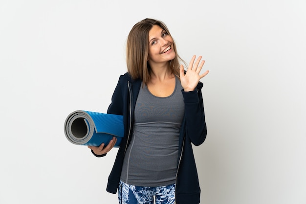 Chica eslovaca que va a clases de yoga aislado en la pared blanca saludando con la mano con expresión feliz