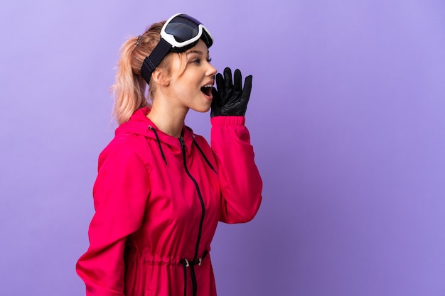 Chica esquiador con gafas de snowboard en púrpura aislado gritando con la boca abierta hacia un lado