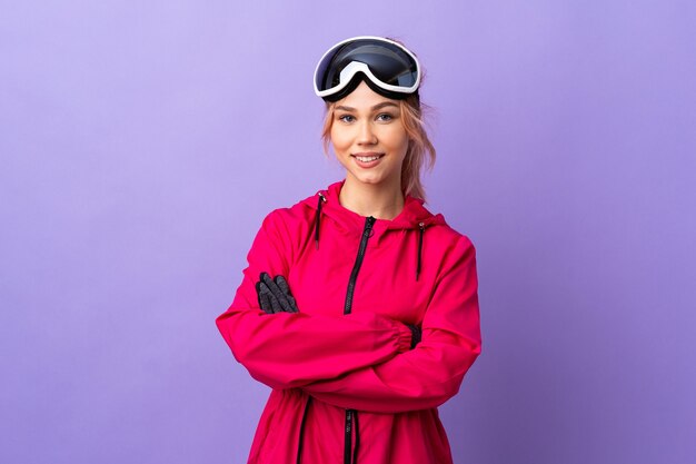Chica esquiador con gafas de snowboard en púrpura aislado manteniendo los brazos cruzados en posición frontal