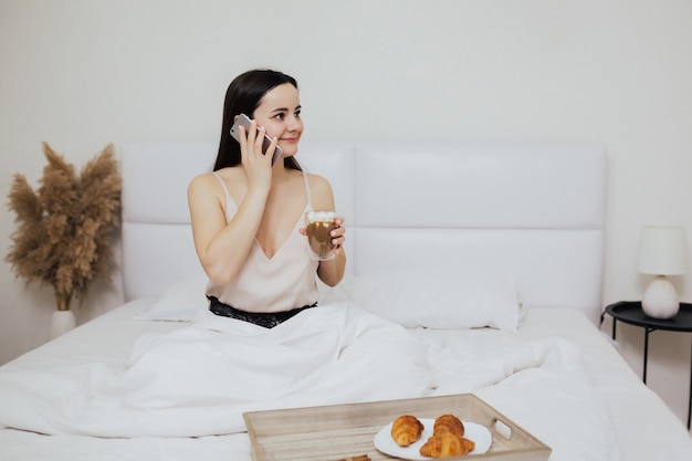 Chica está desayunando y hablando por teléfono en la cama