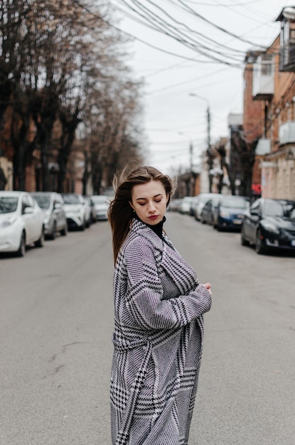 La chica está parada en la calle con un abrigo gris.