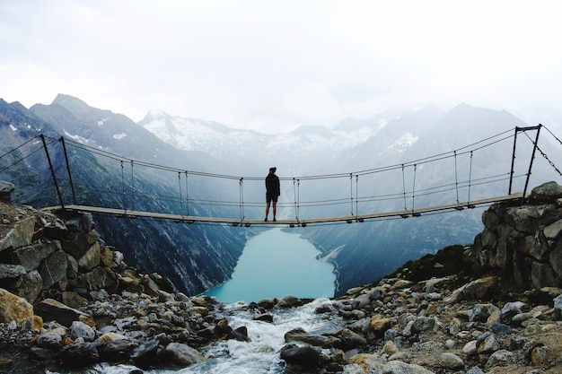 La chica está de pie en un puente mirando a las montañas
