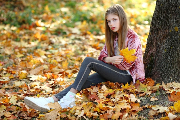 La chica está sentada cerca de un gran árbol en el parque de otoño