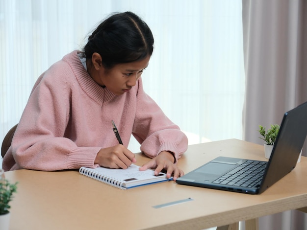 Una chica está sentada en un escritorio con una computadora portátil y un cuaderno