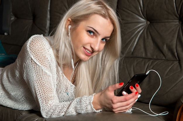 Chica está sonriendo y escuchando música en el sofá