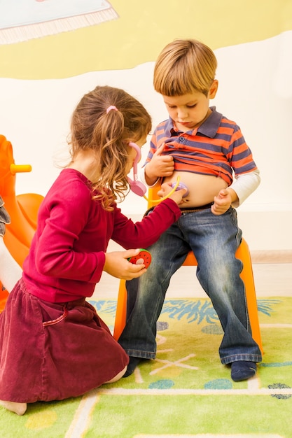 Foto chica con estetoscopio está jugando en un médico y escuchando el vientre del niño