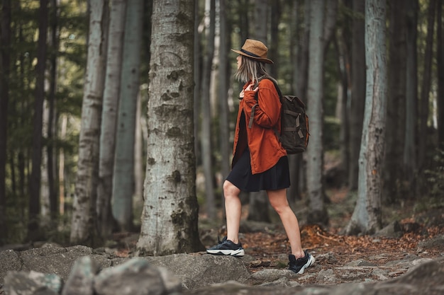 Chica de estilo con sombrero con mochila en un horario de verano Bosque de coníferas mixto