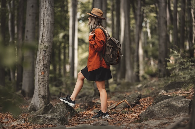 Chica de estilo con sombrero con mochila en un horario de verano Bosque de coníferas mixto