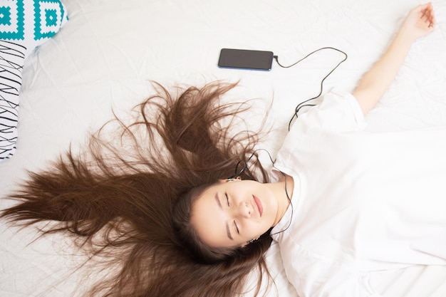 Chica de estilo de vida escuchando música en casa con un teléfono inteligente acostado en la cama