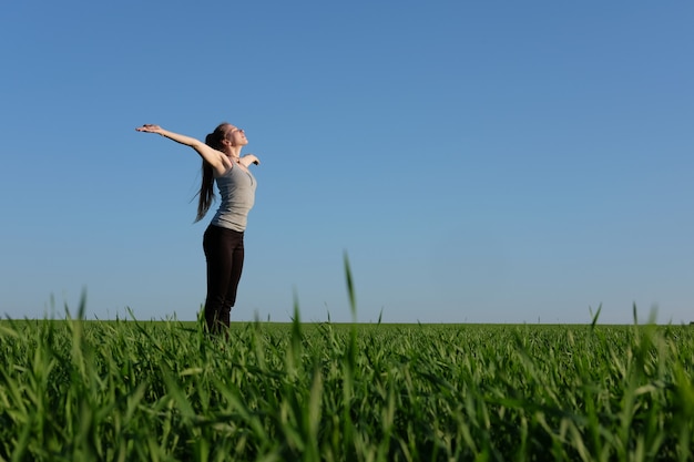 Chica estirarse en campo verde con cielo azul