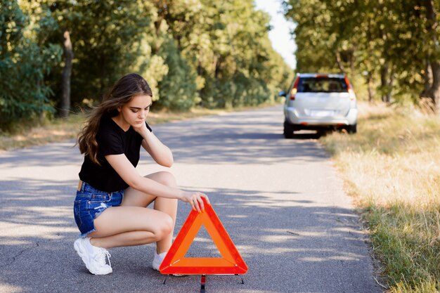 Chica estresada poniendo señal de emergencia en la carretera