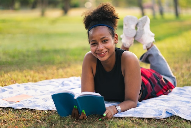 Chica estudiante acostarse y leer un libro en el parque