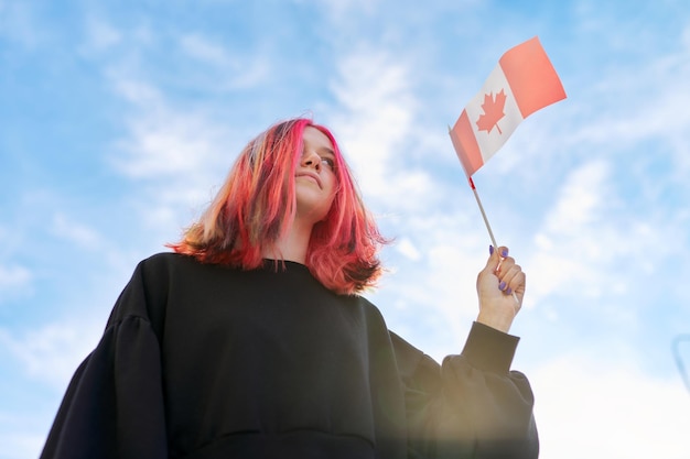 Chica estudiante adolescente con bandera de Canadá en la mano, cielo azul con fondo de nubes. canadá, educación, y, juventud, patriotismo, gente, concepto