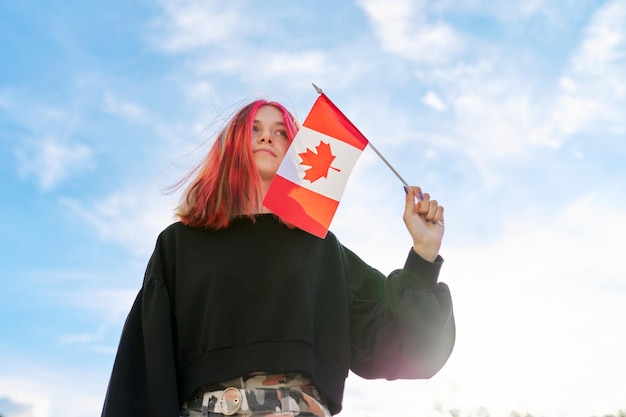 Chica estudiante adolescente con bandera de Canadá en la mano, cielo azul con fondo de nubes. canadá, educación, y, juventud, patriotismo, gente, concepto